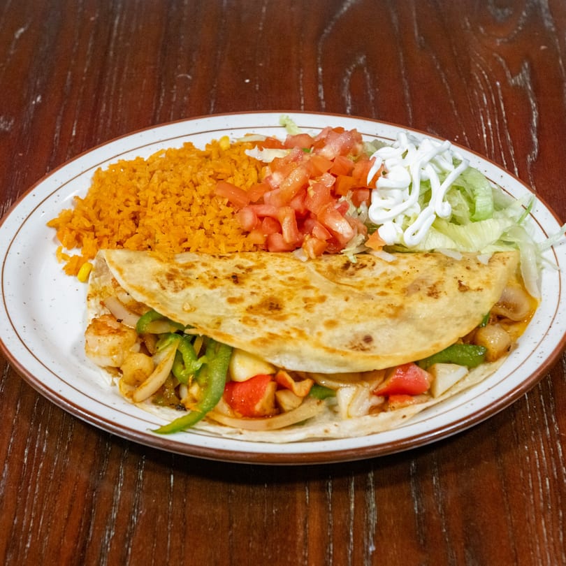 Shrimp quesadilla with bell peppers and onions, served with rice, diced tomatoes, and lettuce with sour cream.