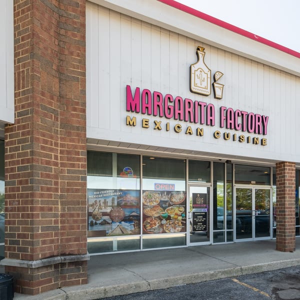 Exterior of Margarita Factory Mexican Cuisine, with a large sign and window displays of food.