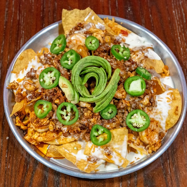 Nachos with ground meat, shrimp, melted cheese, jalapeños, and avocado slices in a metal pan.