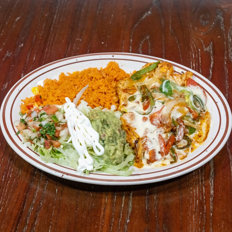 A plate of Mexican food with rice, chicken fajitas, guacamole, pico de gallo, and sour cream.