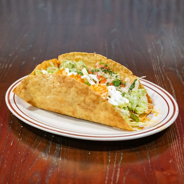 Two golden-fried tacos filled with shrimp, lettuce, guacamole, pico de gallo, and sour cream.