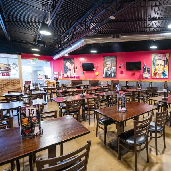 Restaurant dining area with dark wooden tables and chairs, pink walls, and large portraits.