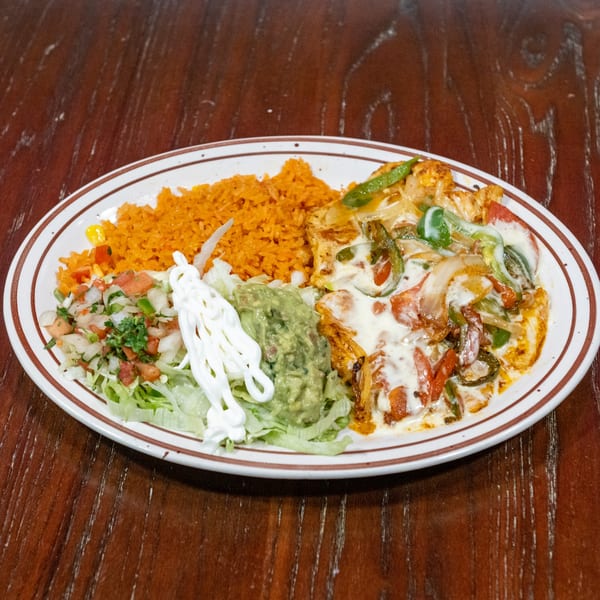 A Mexican dish with rice, fajitas, guacamole, pico de gallo, and sour cream on a white plate.