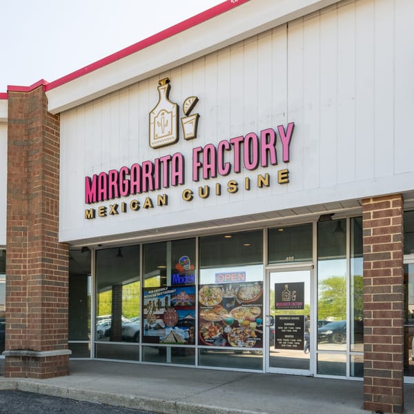 The exterior of Margarita Factory Mexican Cuisine, with a pink and gold sign and menu posters in the windows.