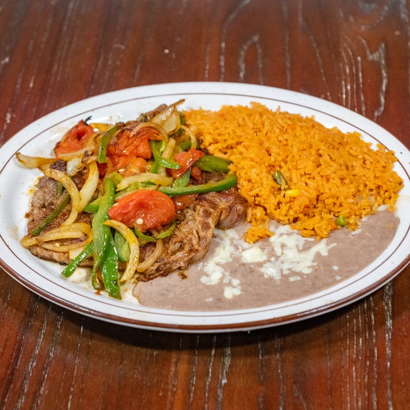 Steak with sautéed onions, bell peppers, and tomatoes, served with rice and refried beans.