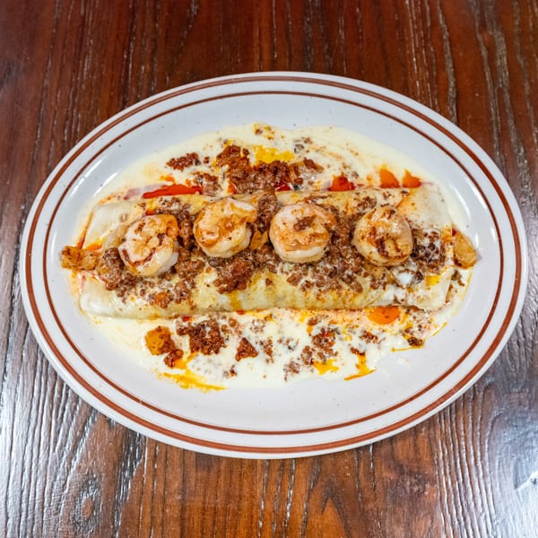 A white oval plate with a burrito covered in white sauce, ground meat, and shrimp.