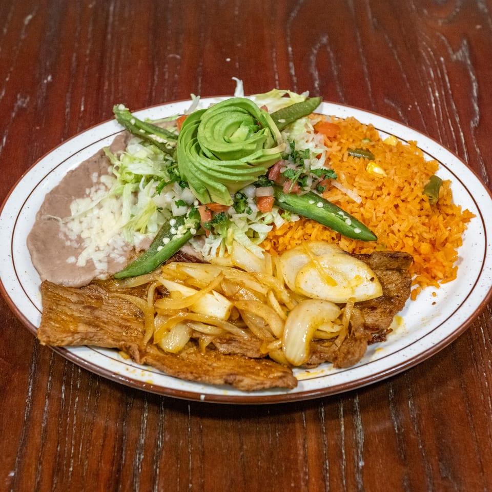 A Mexican dish with steak and onions, rice, refried beans, and a salad with avocado.