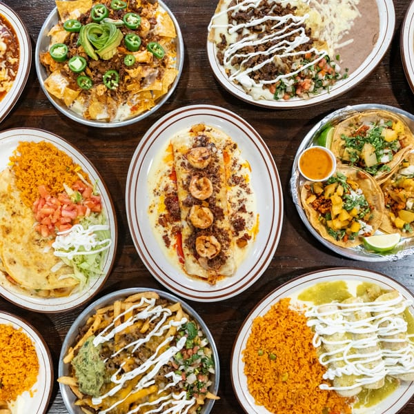 Overhead view of a wooden table laden with various Mexican dishes, including nachos, tacos, and burritos.
