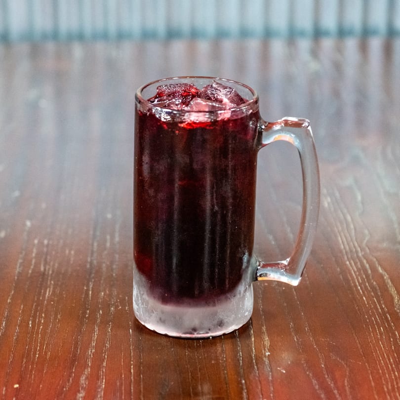 A frosty mug of dark red sangria with ice and fruit sits on a wooden table.