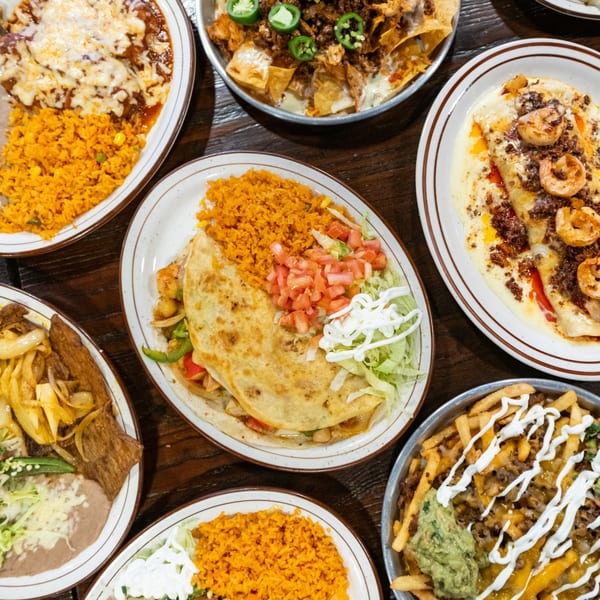 An overhead view of a wooden table laden with various Mexican dishes, including quesadillas, enchiladas, and nachos.