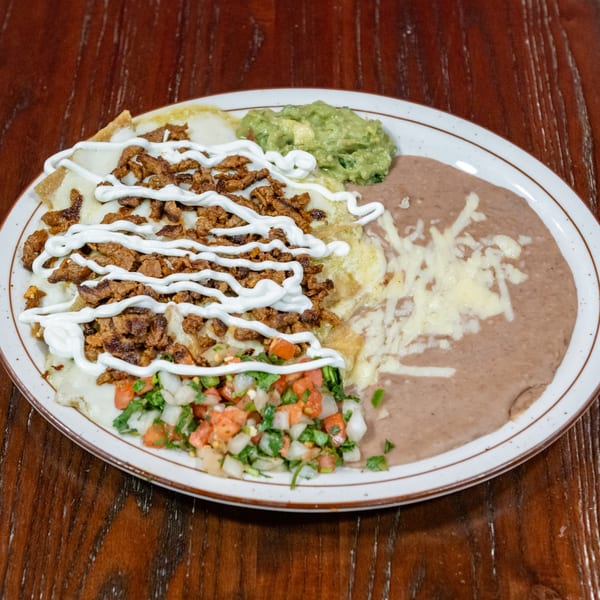 A plate of cheesy enchiladas topped with meat, sour cream, pico de gallo, guacamole, and refried beans.