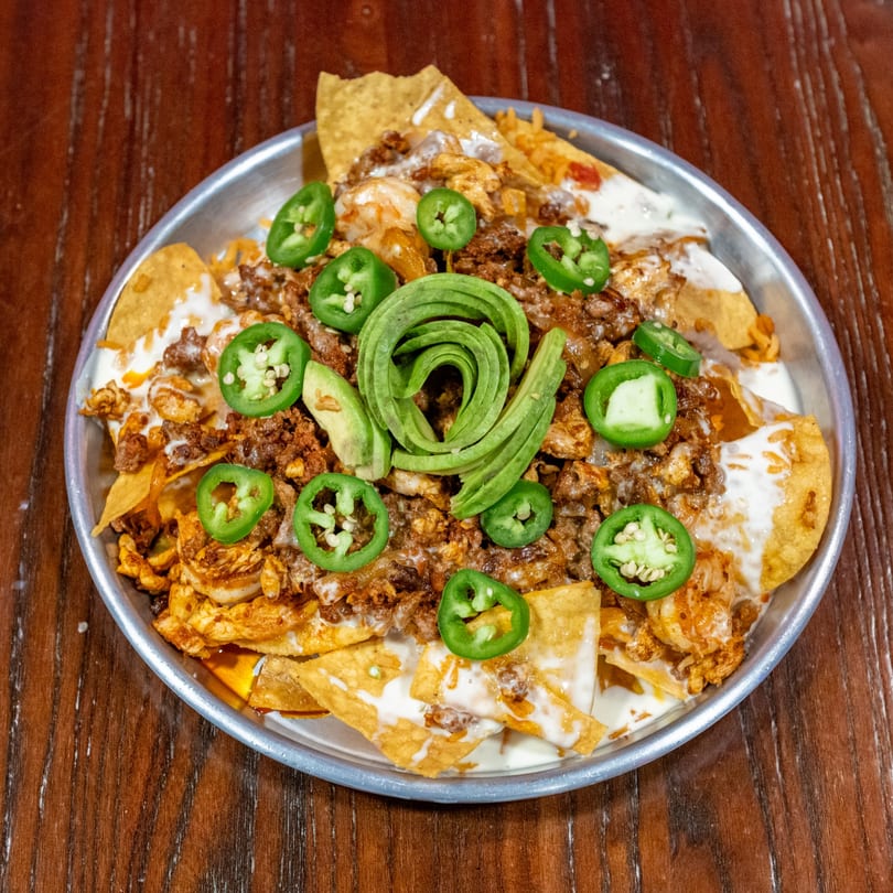 A metal plate of nachos with ground beef, shrimp, jalapeños, and a spiral of avocado.