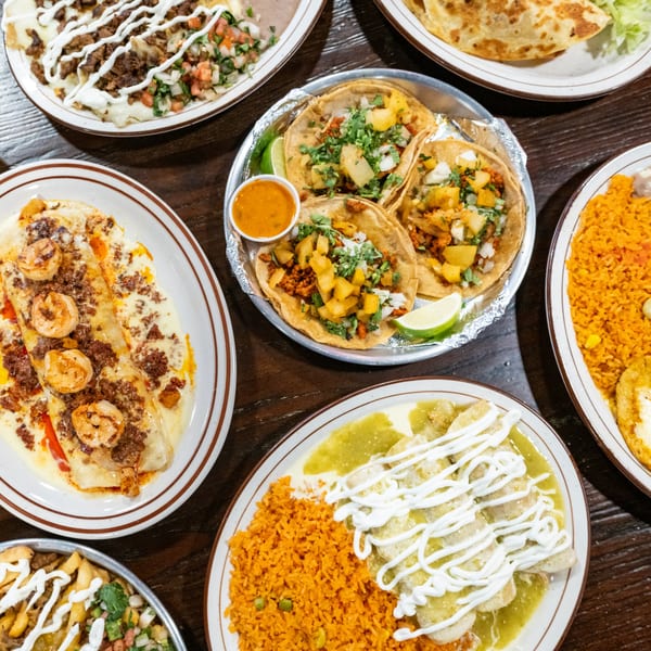 A top-down view of a wooden table laden with various Mexican dishes, including tacos, enchiladas, and rice.
