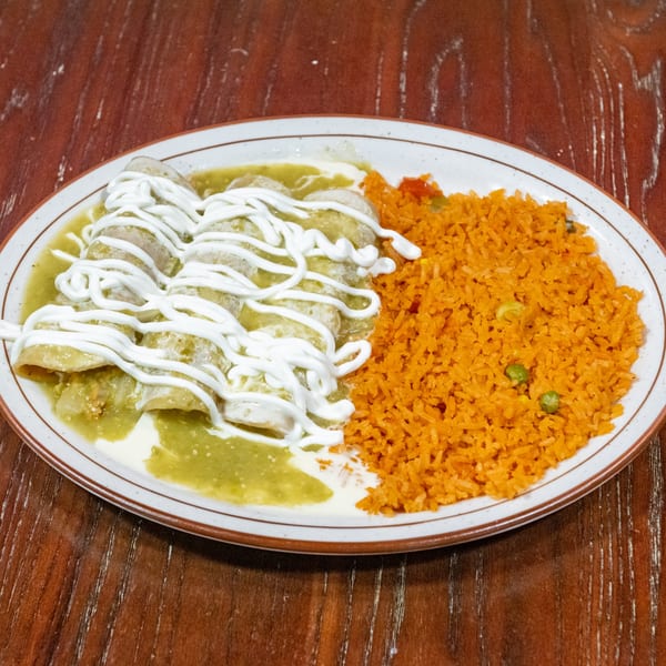Green enchiladas drizzled with sour cream, served with a side of orange rice and peas.