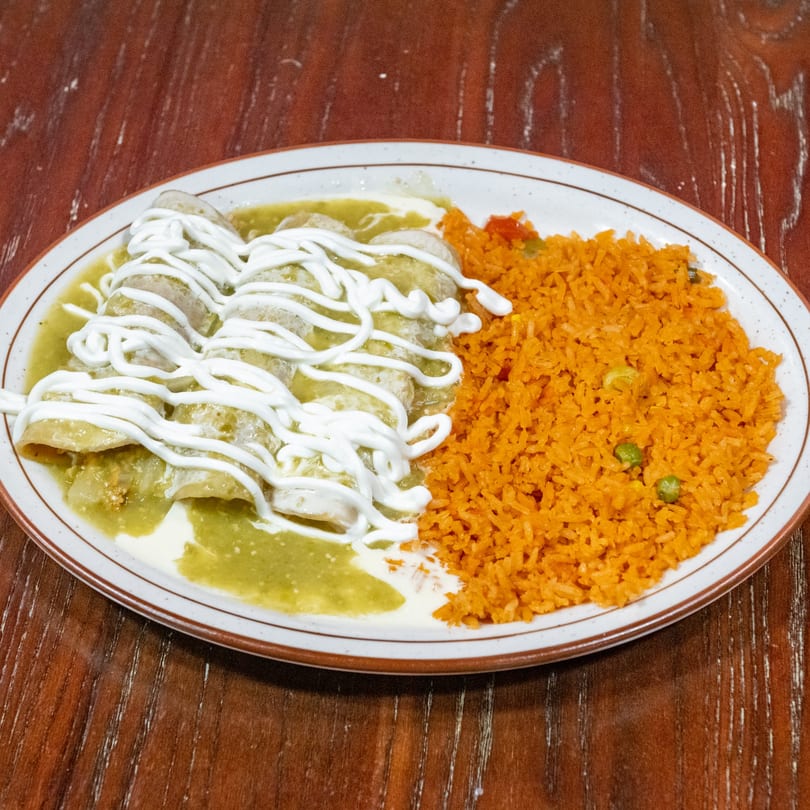Green enchiladas drizzled with sour cream, served with a side of orange rice and peas.
