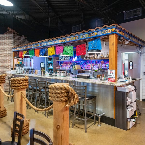 Colorful Mexican restaurant bar with stools, festive papel picado banners, and a tiled roof.