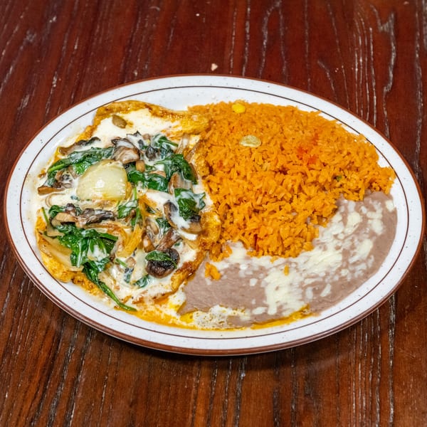 A plate of huevos rancheros with creamy spinach and mushrooms, orange rice, and refried beans.