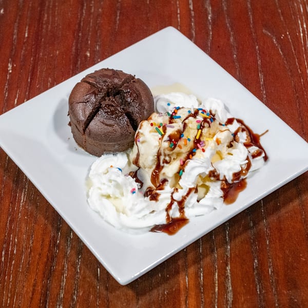 Chocolate lava cake with vanilla ice cream, whipped cream, chocolate syrup, and sprinkles on a white plate.